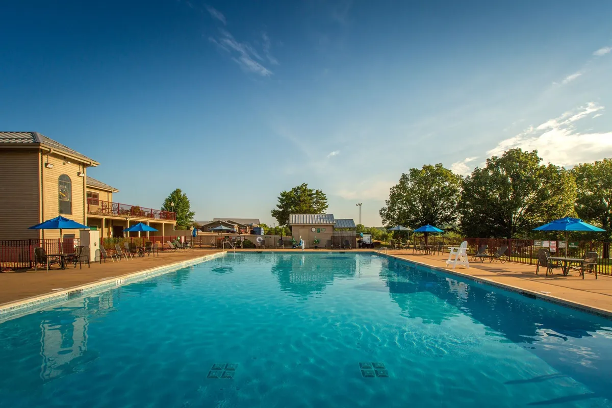 A vibrant outdoor swimming pool surrounded by blue umbrellas, deck chairs, and lush greenery. The pool area looks refreshing and inviting, perfect for relaxing in the sun, socializing, or taking a dip after a day of outdoor adventure.