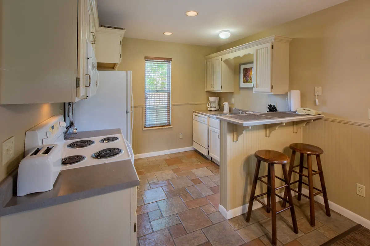 A spacious and modern kitchen with a central island, bar stools, and a large window that allows in natural light. The stove and countertops are visible, providing a clear sense of the fully equipped kitchen space, ideal for cooking and socializing.